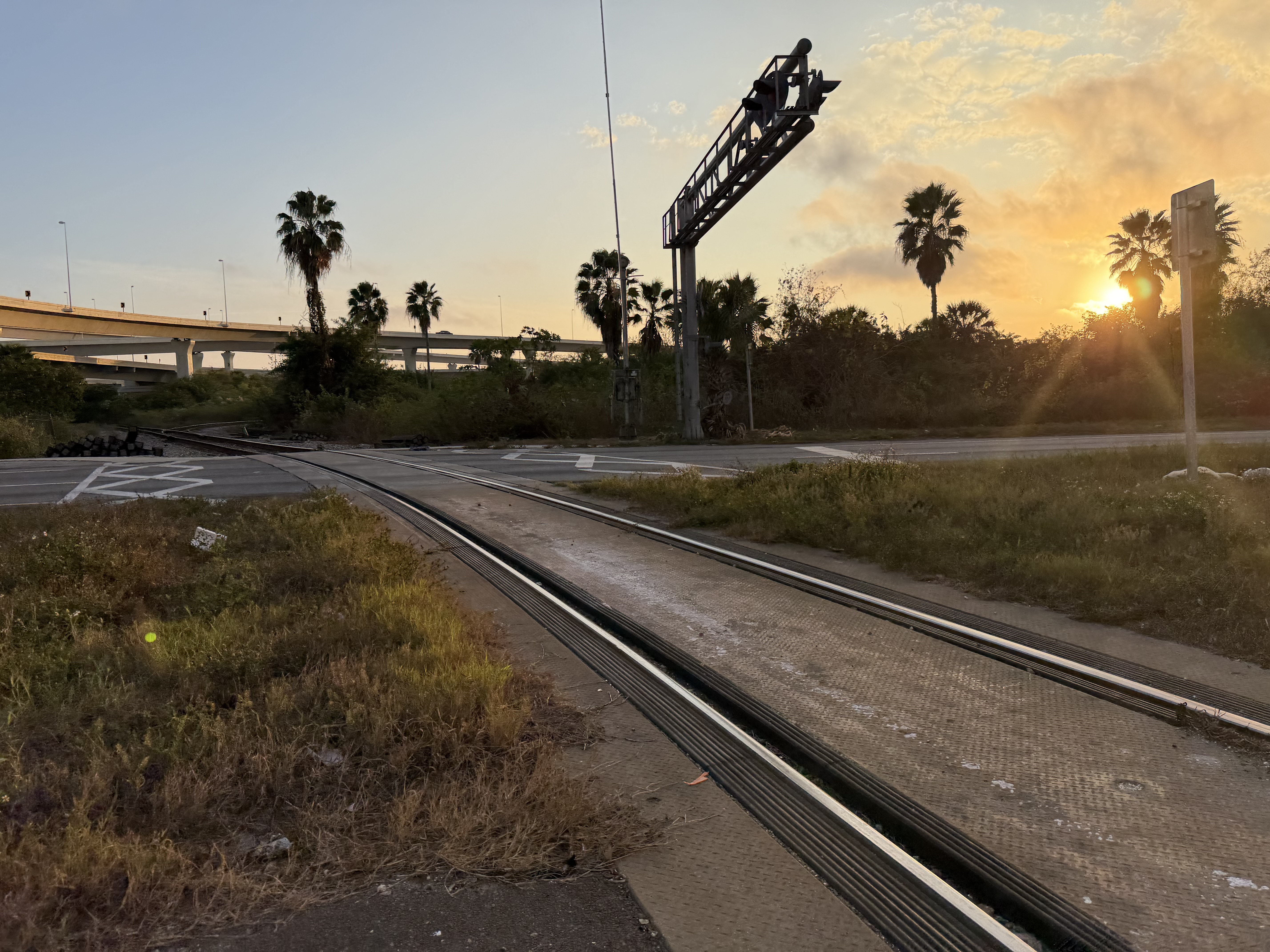 Grade crossing signal cantilever structure at sunset with rail tracks and highway overpass