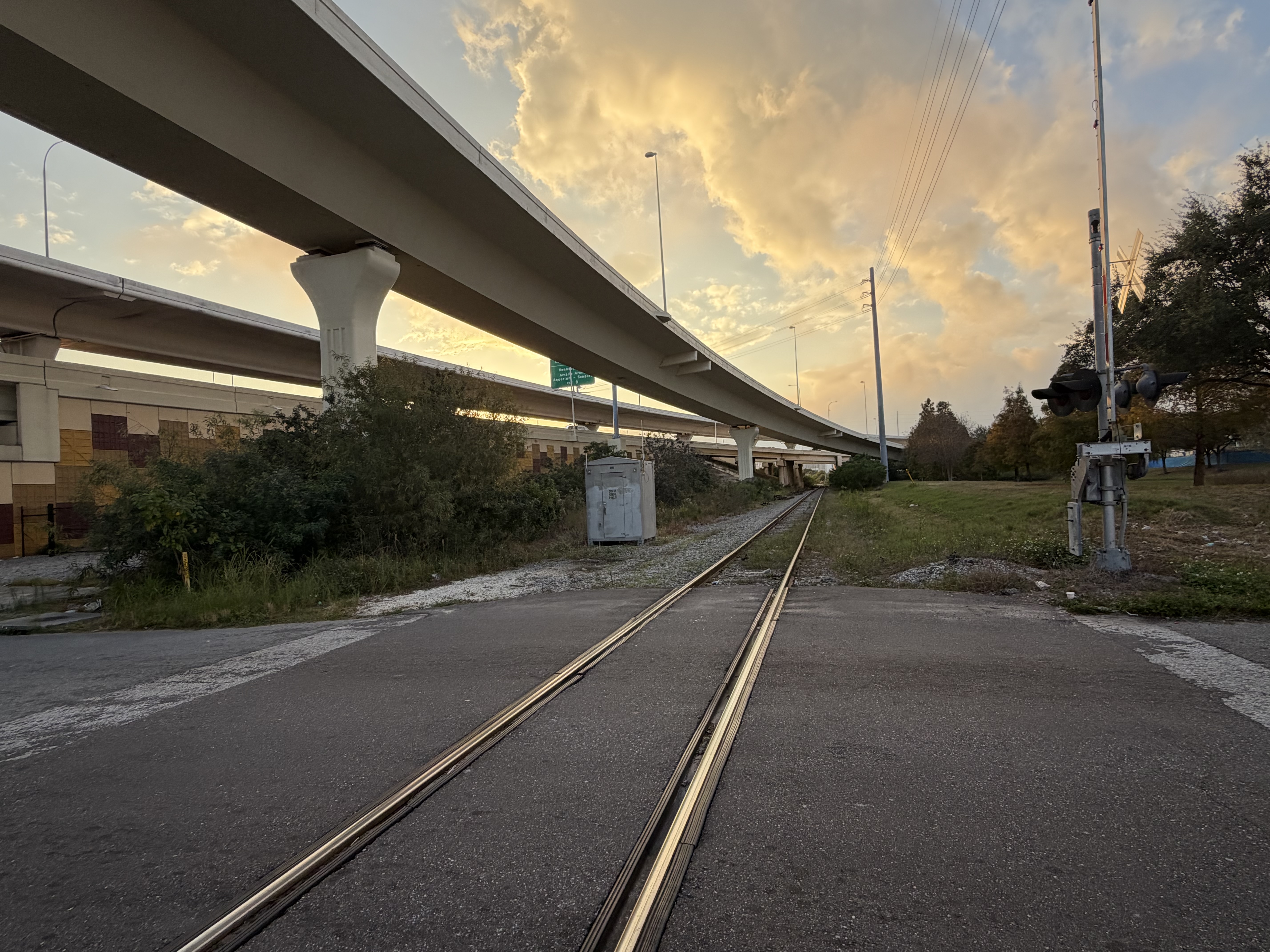 Rail tracks extending into distance at sunset with overhead highway structure and signal equipment
